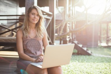 Tatildeki güzel genç bir kadının portresi. O, güneşteki ahşap kulübenin arka planında oturuyor. Turizm ve eğlence sektörü. Modern teknolojiler. Seyahat ve kablosuz iletişim. Doğa ve sükunet. Gençlik ve güzellik.
