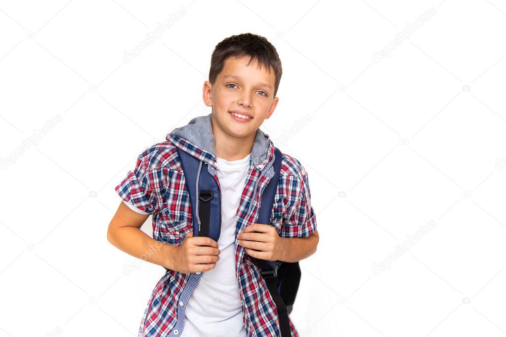 Boy teenager 11 years old schoolboy looking at camera on white background with backpack and smiling. Dressed in plaid shirt and white t-shirt