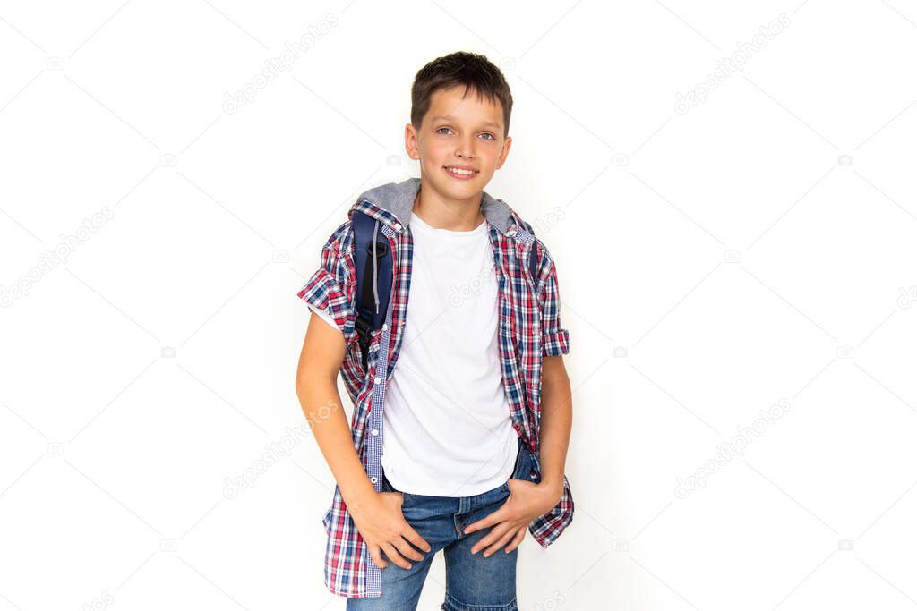 Boy teenager 11 years old schoolboy looking at camera on white background with backpack and smiling. Dressed in plaid shirt and white t-shirt, copy space