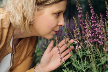 Young woman is happy to smell fragrant flowers on street window of flower shop. Work of florist. Aromatherapy. Medicinal herbs and plants.