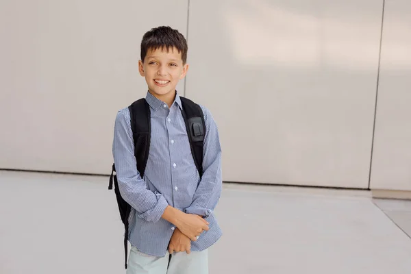 Ragazzo adolescente 11 anni scolaro guardando la macchina fotografica su sfondo grigio con zaino e sorridente. Vestita con camicia a quadri — Foto Stock