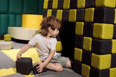 Little boy is concentrating on building house out of soft play blocks while in training children's center. Educational games. Children's problems. Learning through game. Working with autism. 