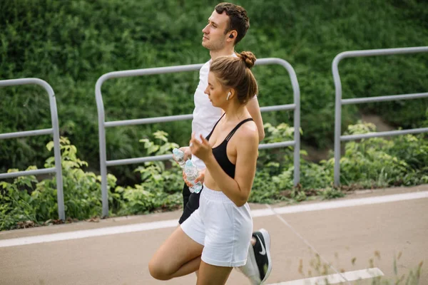 Joven pareja feliz corriendo en el parque de la ciudad con una botella de agua en las manos, deportes conjuntos, alegría, deporte de la ciudad estilo de vida saludable, fitness juntos — Foto de Stock