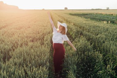 Tarlalarda yürürken genç ve güzel bir kadın elini sallayarak giden güneşe veda ediyor. Hamilelik bakımı. Güzellik ve sağlık. Mutluluk ve sükunet. Sağlıklı yaşam tarzı.