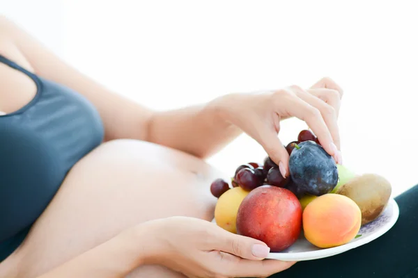 Pregnant woman and fruits on plate — Stock Photo, Image