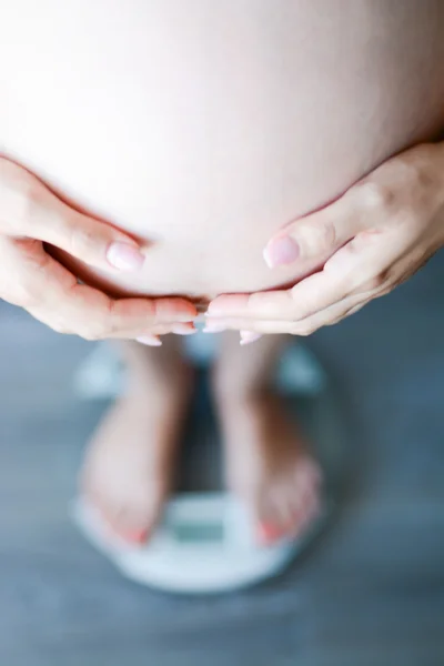 Kobieta w ciąży dotykając brzuch na skali — Zdjęcie stockowe