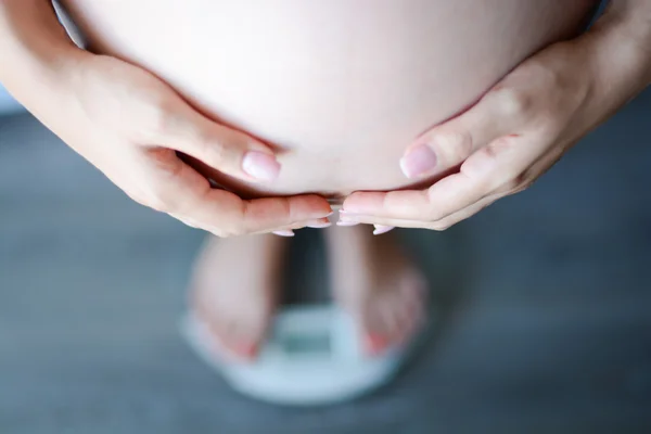 Pregnant woman touching belly on scale — Stock Photo, Image