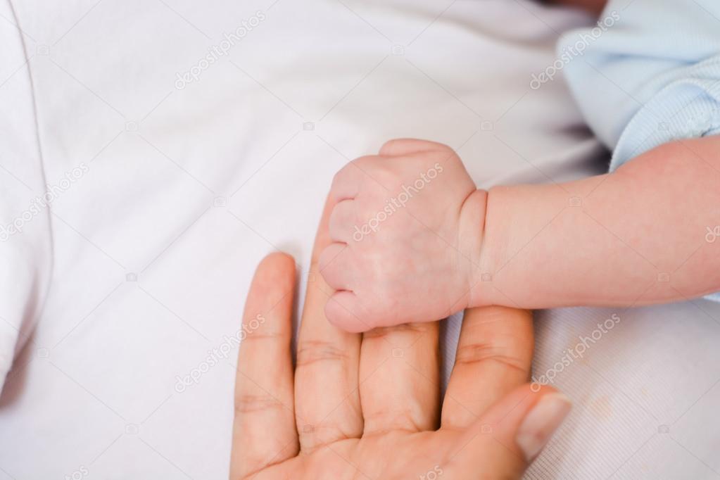 Baby holding finger of mother