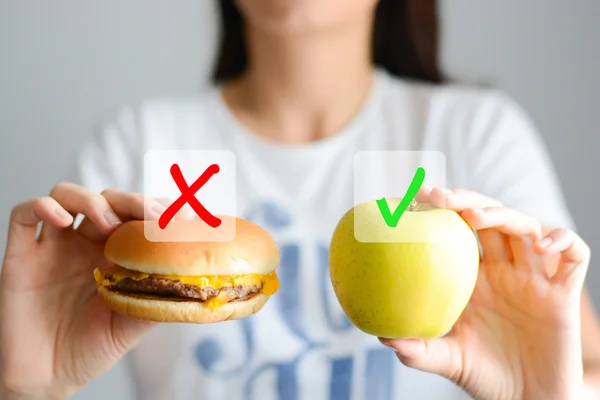 young woman holding hamburger and apple