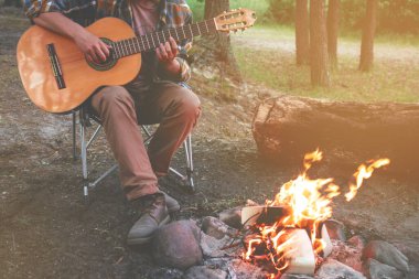 Ormanda kamp yapmak. İnsan doğada ateşin yanında gitar çalar. Yaz kampı. Doğada rahatlama