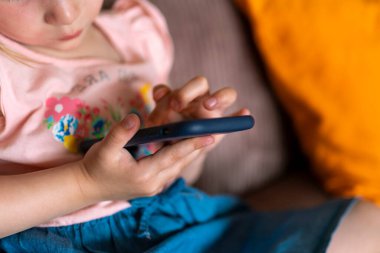 Sarışın bir kız evde akıllı telefonuyla oynuyor. Çocuk ve akıllı telefon ellerinde. Dijital tabletli çocuklar