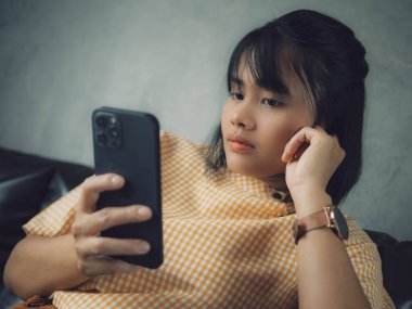 Akıllı telefon kullanan bir kadın, rahat bir evde oturan genç bir hippi kız ve modern akıllı telefon cihazı kullanan, elinde siyah bir dokunmatik telefon tutan bir kadın. Sosyal ağ oluşturma kavramı.