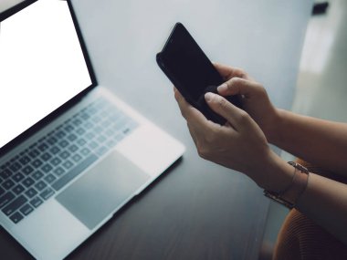 Evde dizüstü bilgisayar ve akıllı telefon kullanan Asyalı kadın. Genç Asyalı iş kadını akıllı telefondan bahsediyor ve labaratuvarla çalışıyor. Ev konsepti üzerine çalışıyor..