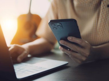 Evde dizüstü bilgisayar ve akıllı telefon kullanan Asyalı kadın. Genç Asyalı iş kadını akıllı telefondan bahsediyor ve labaratuvarla çalışıyor. Ev konsepti üzerine çalışıyor..