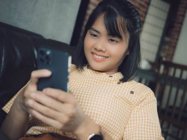 Akıllı telefon kullanan bir kadın, rahat bir evde oturan genç bir hippi kız ve modern akıllı telefon cihazı kullanan, elinde siyah bir dokunmatik telefon tutan bir kadın. Sosyal ağ oluşturma kavramı.