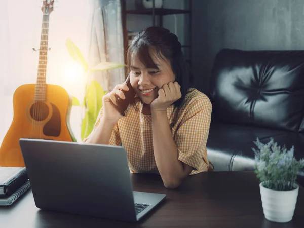 Evde dizüstü bilgisayar ve akıllı telefon kullanan Asyalı kadın. Genç Asyalı iş kadını akıllı telefondan bahsediyor ve labaratuvarla çalışıyor. Ev konsepti üzerine çalışıyor..