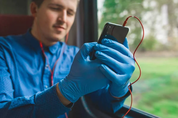 A guy in protective medical gloves sits on the phone and listens to music, close-up