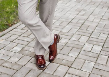 Adamın bacakları, açık renk pantolonlar ve kahverengi ayakkabılar içinde, kaldırım taşları üzerinde ayakta duruyor..