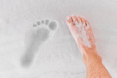 Erkeklerin bacakları sahildeki kumların üzerinde ayak izlerinin yanında duruyor..