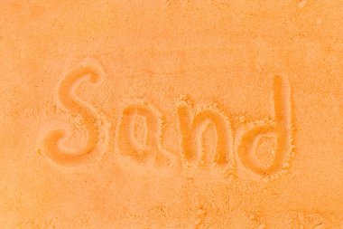 Kum kelimesi turuncu bir kumsal arka planında yazılıdır. Kum kavramının işareti veya sembolü.