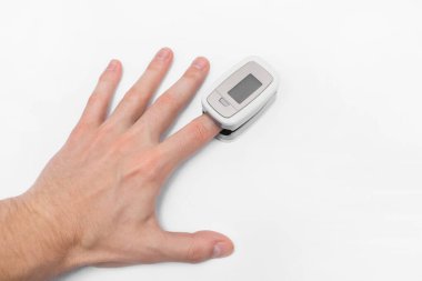 Adamın eli, beyaz bir arka planda modern bir tıbbi cihazla doygunluğu ölçüyor..