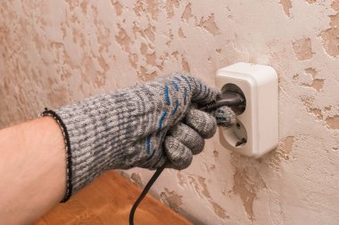 Koruyucu eldivenli bir inşaat işçisinin eli modern bir odanın arka planına çift prizle bağlı..