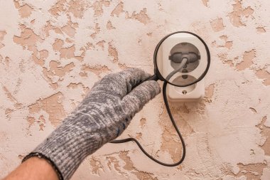 Koruyucu eldivenli bir inşaat işçisinin eli evdeki aletlerin bağlantısını büyüteçle inceliyor..