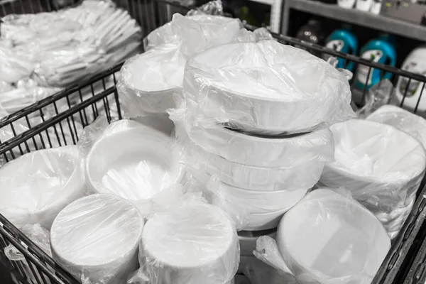 A set of white disposable plastic tableware in cellophane packaging in a store.