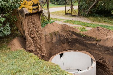 İçinde kum ve toprak yığını olan bir kova kazıcı sanayi bölgesine beton halkalar gömüyor..