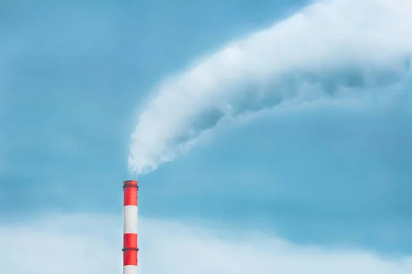 Environmental pollution, ecological problem, smoke from a pipe of a thermal power plant against a blue sky.