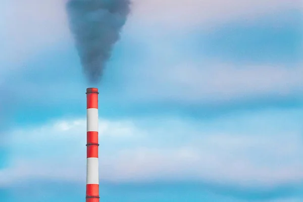 Environmental pollution, environmental problem, smoke from the pipe of an industrial plant or thermal power plant against a blue sky.