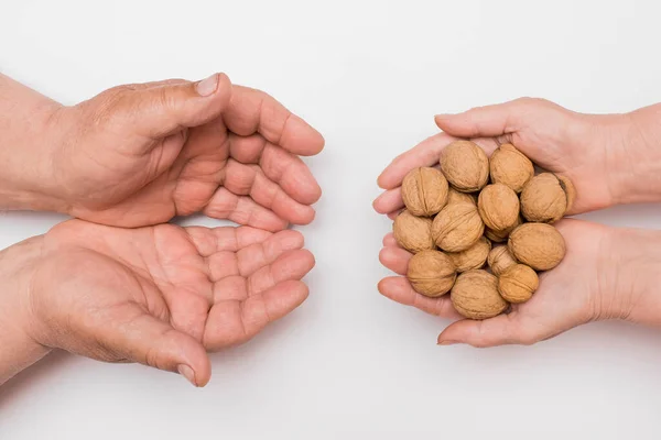 Hands of an elderly woman pass a bunch of whole walnuts into the hands of an elderly man isolated on white background. Care and attention concept.
