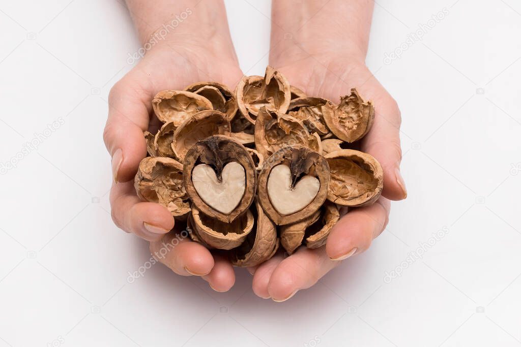 Woman holds out her hands with a bunch of peeled shell and two halves of a walnut in the form of a heart on a white background, isolated. Nut concept.