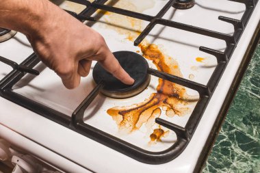 Adamın eli, mutfakta ev yemeği yaptıktan sonra gaz ocağındaki kirli plaketi işaret ediyor..