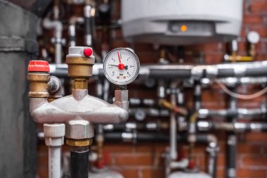 Bir endüstriyel işletmedeki ısıtma ünitesinin arka planına karşı boruda otomatik emniyet vanası olan bir basınç göstergesi..