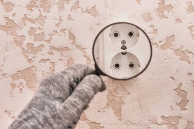 Koruyucu eldivenli bir inşaat işçisinin eli evdeki aletlerin bağlantısını büyüteçle inceliyor..