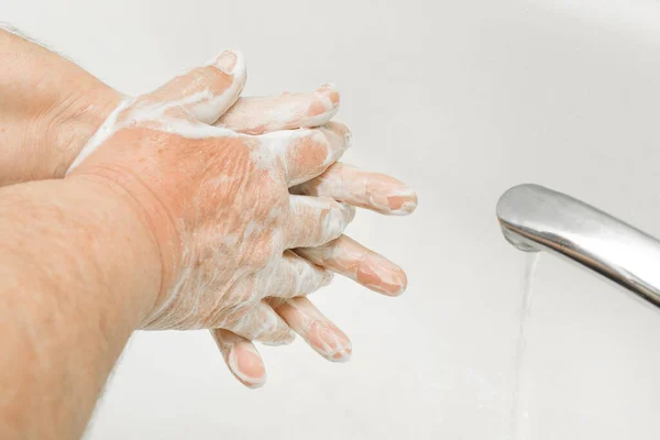 Elderly man washes hands with soap under the tap in the bathroom close-up, recommendation for frequent handwashing, domestic hygiene.