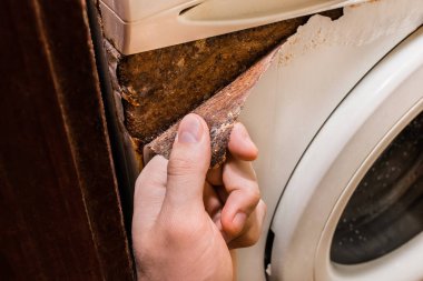 Eski bir çamaşır makinesinin paslı kabuk soyma tabakasını tutan eller..