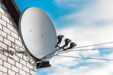 Beyaz tuğlalı duvardaki uydu anteni bulutlu mavi gökyüzüne karşı..