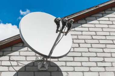 Mavi gökyüzüne karşı beyaz tuğlalı bir duvardaki uydu anteni..