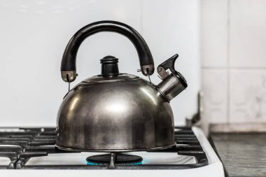 Islık çalan metal bir çaydanlık mutfaktaki gaz sobasında suyu kaynayana kadar ısıtır..