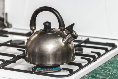 Islık çalan metal bir çaydanlık mutfaktaki gaz sobasında suyu kaynayana kadar ısıtır..