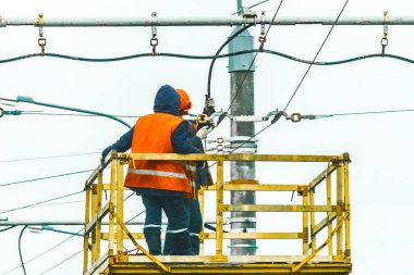 Çalışan iki adam bir vinç teçhizatında güvenliği artırdı. Elektrik hattını tamir ediyorlardı..