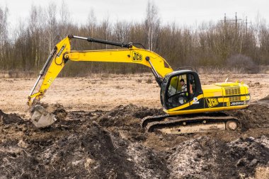 Belarus, Minsk bölgesi - 11 Aralık 2019: Sürüngen kazıcı teçhizatındaki inşaat işçisi sanayi bölgesinde hendek kazıyor. Toprak ve toprakla kazı çalışmaları.