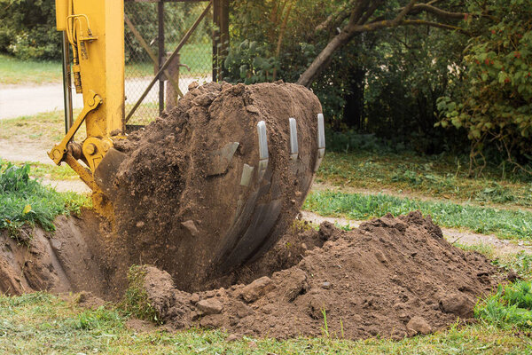 A bucket of a bulldozer with a pile of land next to a pit in an industrial zone. Excavation work.