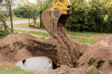 İçinde kum ve toprak yığını olan bir kova kazıcı sanayi bölgesine beton halkalar gömüyor..