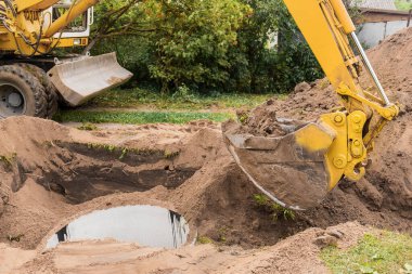 İçinde kum ve toprak yığını olan bir kova kazıcı sanayi bölgesine beton halkalar gömüyor..
