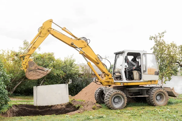 Kazı makinesinin hidrolik piston sistemi çelik kablolardaki beton kanalizasyon şebekesinin çukuruna iniyor. Kanalizasyon evinin inşaatı veya onarımı.
