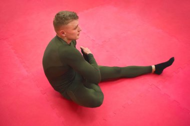 Yeşil termal takım elbiseli genç sporcu spor salonunda egzersiz yapıyor..