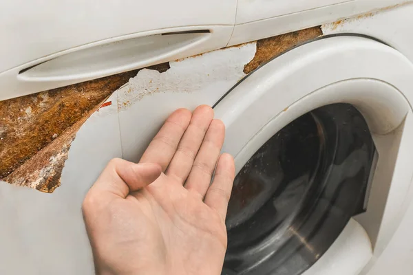 A man\'s hand points a fingers at a trace of rust next to the front keypad of an old broken washing machine. Home appliances wear concept.